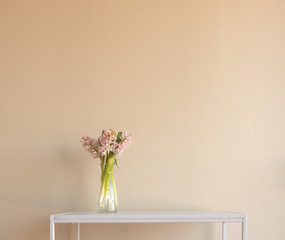 Soft pink hyacinths in glass vase on white contemporary table against beige wall (selective focus)