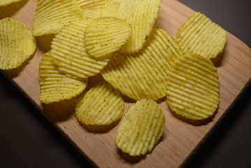 Potatoes fried wavy, embossed, potato chips with sour cream and greens, facies on a wooden board