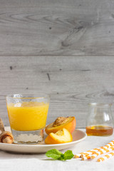 Peach smoothie in glass on a plate with fresh peaches, honey and mint. Healthy beverage. Breakfast or snack. Copy space