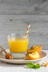 Peach smoothie in glass on a plate with fresh peaches, honey and mint. Healthy beverage. Breakfast or snack. Copy space