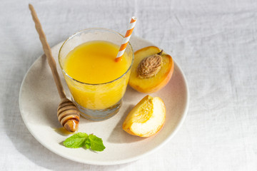 Peach smoothie in glass on a plate with fresh peaches, honey and mint. Healthy beverage. Breakfast or snack. Copy space