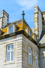 View of the top of a residential building in the old city of Saint-Malo in Brittany, France, with a slate roof covered with lichen, dormer windows and large chimneys against blue sky.