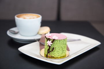 Mousse dessert with basil and strawberry flavour on a white plate and a cup of cappucino 