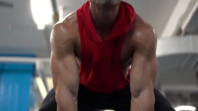 Young handsome athlete lifting barbell at the gym. Attractive guy with perfect muscular body in red t-shirt is in training. Sexy bodybuilder doing doing gym workout