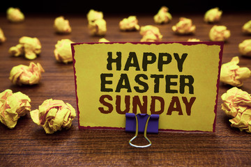 Handwriting text writing Happy Easter Sunday. Concept meaning Greeting someone about holidays Spring is coming Yellow sticky card clipped text notice crumpled paper balls wood table.