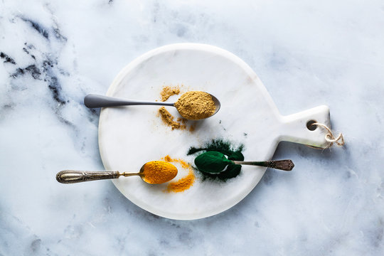 ginger and turmeric powder and hawaiian spirulina in tablespoons on the board and white marble table. healthy supplements, superfoods in cooking