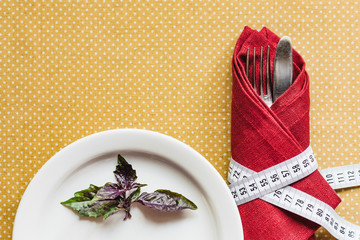 Red basil on a plate; fork and knife are tied with a measuring tape. View from above. The concept of diet and weight loss.