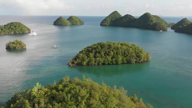 Drone shot of tropical islands or islet with a boat on the background floating towards the horizon.