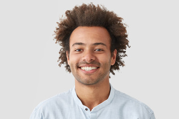 Mixed race curly male with broad smile, shows perfect teeth, being amused by interesting talk, has...