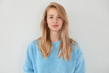 Adorable blonde female with serious expression, dressed in blue sweater, has healthy clean skin, isolated over white background. Pretty woman demonstrates her natural beauty. People and youth