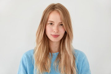 Horizontal shot of pleasant looking European female with satisfied expression, has lovely appearance, dressed in casual blue sweater, isolated over white background. People and tenderness concept