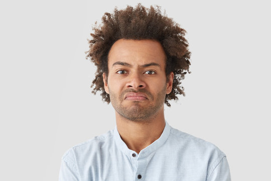 Negative human facial expressions concept. Curly African American male purses lips, has angry look, being dissatisfied with not delicious supper cooked by wife, suggests go in restaurant instead