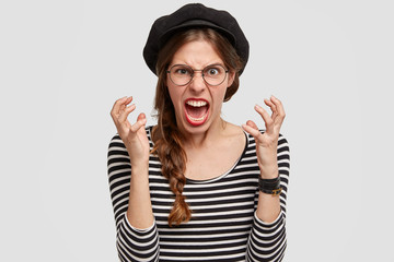 Negative human feelings. Angry annoyed young female from France, shouts angrily, gestures with hands, stares in irritation, being displeased by negative comments, stands against white background