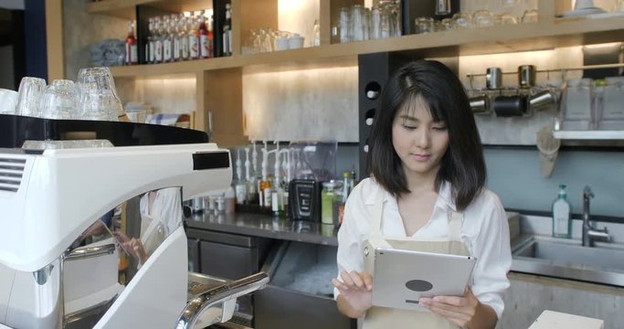 Young asian barista using tablet computer during a break on the work in the coffee shop.