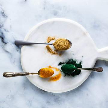 ginger and turmeric powder and hawaiian spirulina in tablespoons on the board and white marble table. healthy supplements, superfoods in cooking