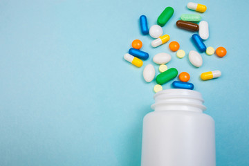 Multi-colored tablets and capsules, white bottle for tablets, pharmaceutical medicine pills on blue background, an analgesic against diseases