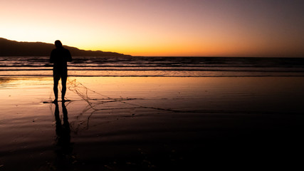 Night fishing silhouette sunset shot on the Kapiti coast beach near Paraparaumu in Wellington area, North Island of New Zealand.