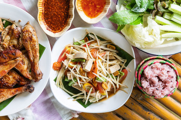 Top view of papaya salad and grilled chicken in white plate on bamboo background