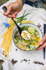 Woman hand holds and eat ramen noodle soup with egg, corn and meat in bowl. Asian Thai traditional authentic food with vegetables served in cafe or restaurant