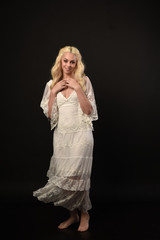 Fototapeta premium full length portrait of blonde girl wearing white lace dress. standing pose. black studio background.