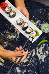 Woman hands holds with chopsticks sushi rolls with tofu, rice, cucumber, avocado, carrot, sour gari - pickled red ginger and wasabi wrapped into nori seaweed. Raw vegan vegetarian healthy food