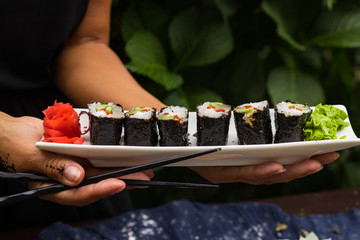 Woman hands holds with chopsticks sushi rolls with tofu, rice, cucumber, avocado, carrot, sour gari - pickled red ginger and wasabi wrapped into nori seaweed. Raw vegan vegetarian healthy food
