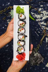Woman hands holds with chopsticks sushi rolls with tofu, rice, cucumber, avocado, carrot, sour gari - pickled red ginger and wasabi wrapped into nori seaweed. Raw vegan vegetarian healthy food