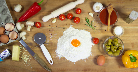 Ingredients for the preparation pizza on wooden background. Flour, eggs, tomatoes, olives, garlic, rosemary ...