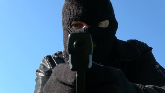 Gangster robber with gun and black mask on sky background