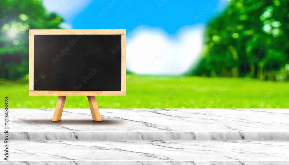 Poster Blank blackboard on white marble table top with blur grass field in park with bokeh light at background,Mock up template for display of your design,Banner for advertise of product,panorama view.