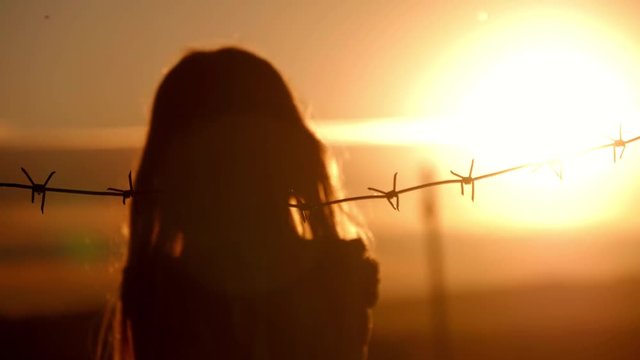 Small girl is at sunset behind barbed wire. The concept of freedom and Immigration.