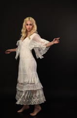 Naklejka premium full length portrait of blonde girl wearing white lace dress. standing pose. black studio background.