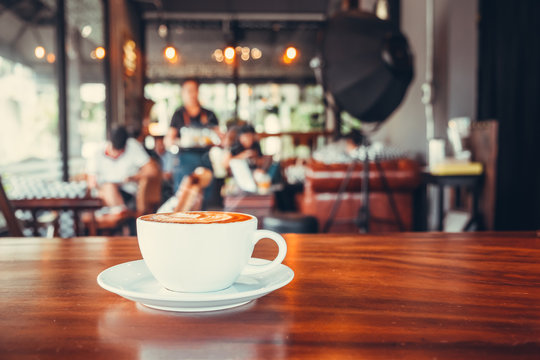 White cup of hot coffee on table in cafe with people. vintage and retro color effect - shallow depth of field