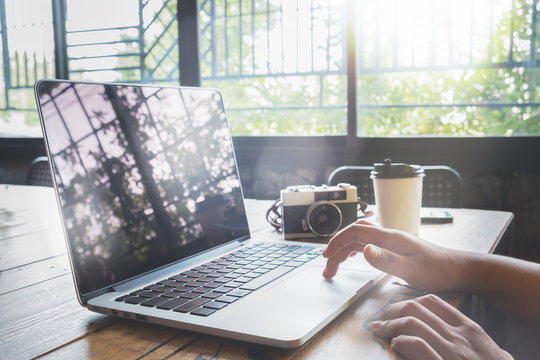Hipster woman traveler using laptop computer in cafe. young woman photographer working at coffee shop. freelance worker concept. Film color tone. Flares and light effect background.