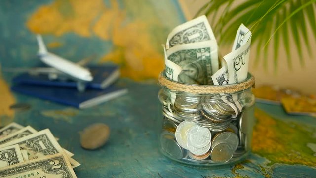 Travel budget concept. Money saved for vacation in glass jar with world map, passport and plane. Banknotes and coins for adventure. Savings for journey. Collecting money for trip. Moneybox with cash.