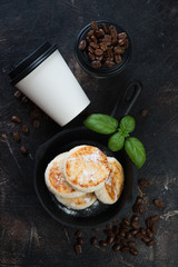 Cheesecakes or syrniki with takeaway coffee for breakfast, flatlay on a dark brown stone background, vertical shot