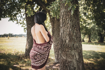 Gypsy girl with long hair posing at nature. A woman with a slim figure and athletic body in knitted sweater, dressed in a sexy kardigan, vintage tones  - obrazy, fototapety, plakaty