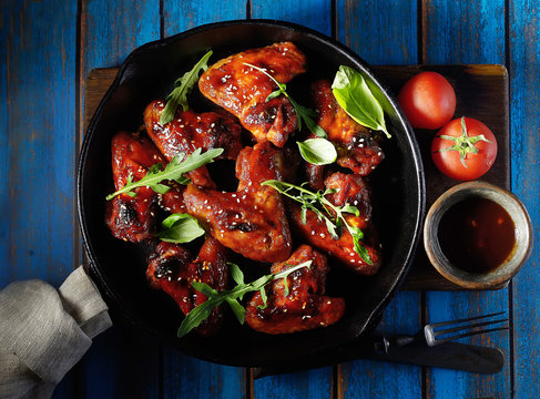 Barbecue on the grill chicken wings in a frying pan on a wooden background