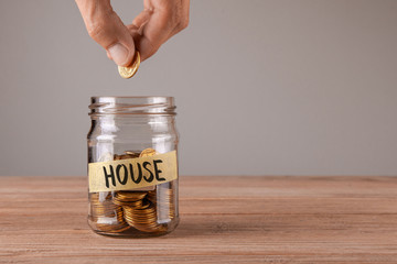 Glass jar with coins and an inscription house. Man holds  coin in hand