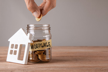 Glass jar with coins and an inscription mortgage and symbol of  house. Man holds  coin in hand