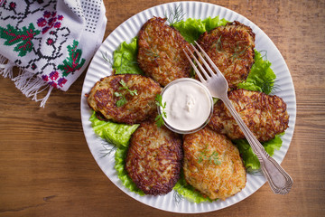 Potato fritters, latkes, draniki, hash browns - popular dish in many countries. Vegetable pancakes on white plate, wooden table. overhead, horizontal