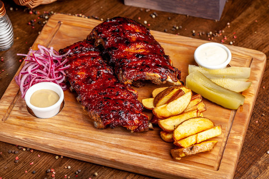 Fried Ribs Air Fryer In Marinade, With Tartar Sauce On A Wooden Board. With French Fries In A Rustic Way And Vegetables. Concept Of A Beautiful Serve In A Restaurant Or In A Cafe.