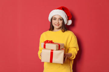 Young woman with Christmas gifts on color background