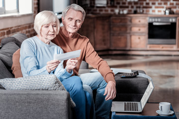 Having rest. Handsome grey-haired man embracing his woman while sitting on the sofa
