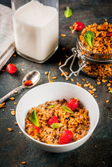Homemade granola from mix of cereals (barley, oat, rye, bran) with with strawberry, mint leaves and fresh organic milk on dark blue concrete background