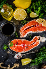 Raw salmon fish steaks with lemon, herbs, olive oil, ready for grill, slate cutting board, dark rusty background copy space