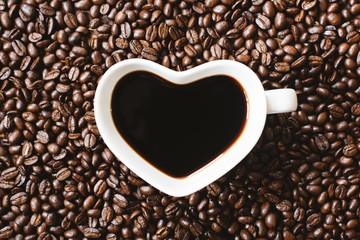 coffee in a heart shape cup on coffee beans background. refreshment and favourite drink concept