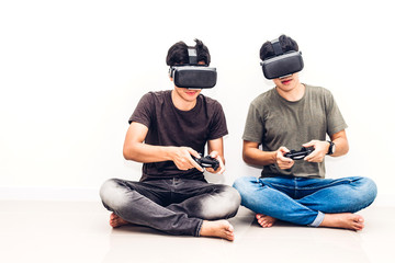 Two friends sitting and enjoying play video game with technology virtual reality together on white wall background at home