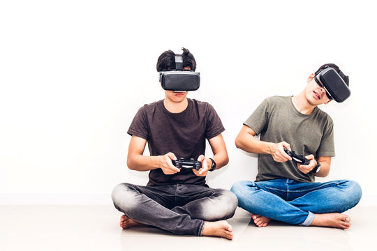 Two friends sitting and enjoying play video game with technology virtual reality together on white wall background at home - Powered by Adobe