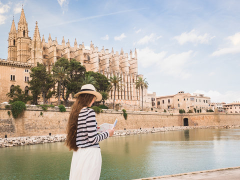 Stylish woman looking at the map with sights on the background of palm trees and historical buildings. Spain, Palma de Mallorca